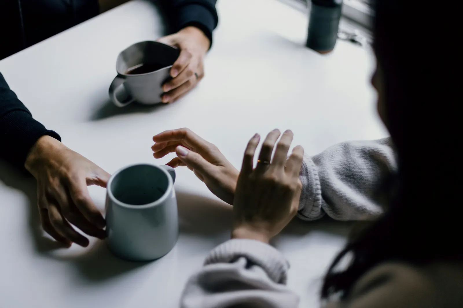 hands reaching for mugs of coffee across a table