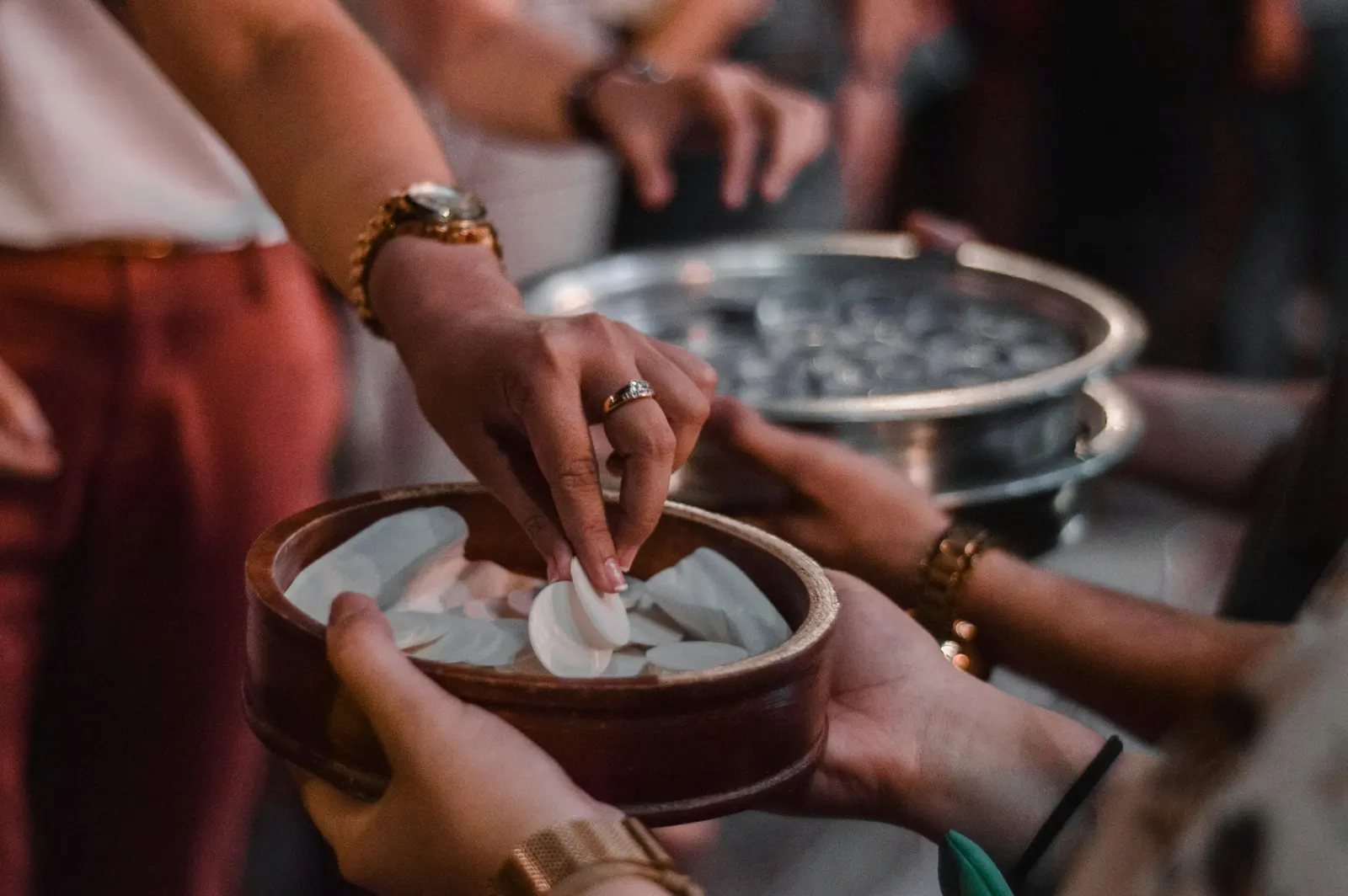 hands taking a communion wafer from a wooden bowl