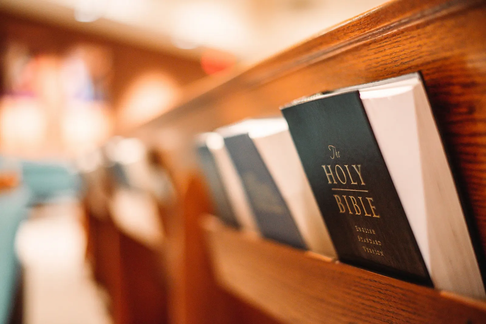 hymnals and Bibles lined up in a wooden pew rack with a softly blurred sanctuary behind them