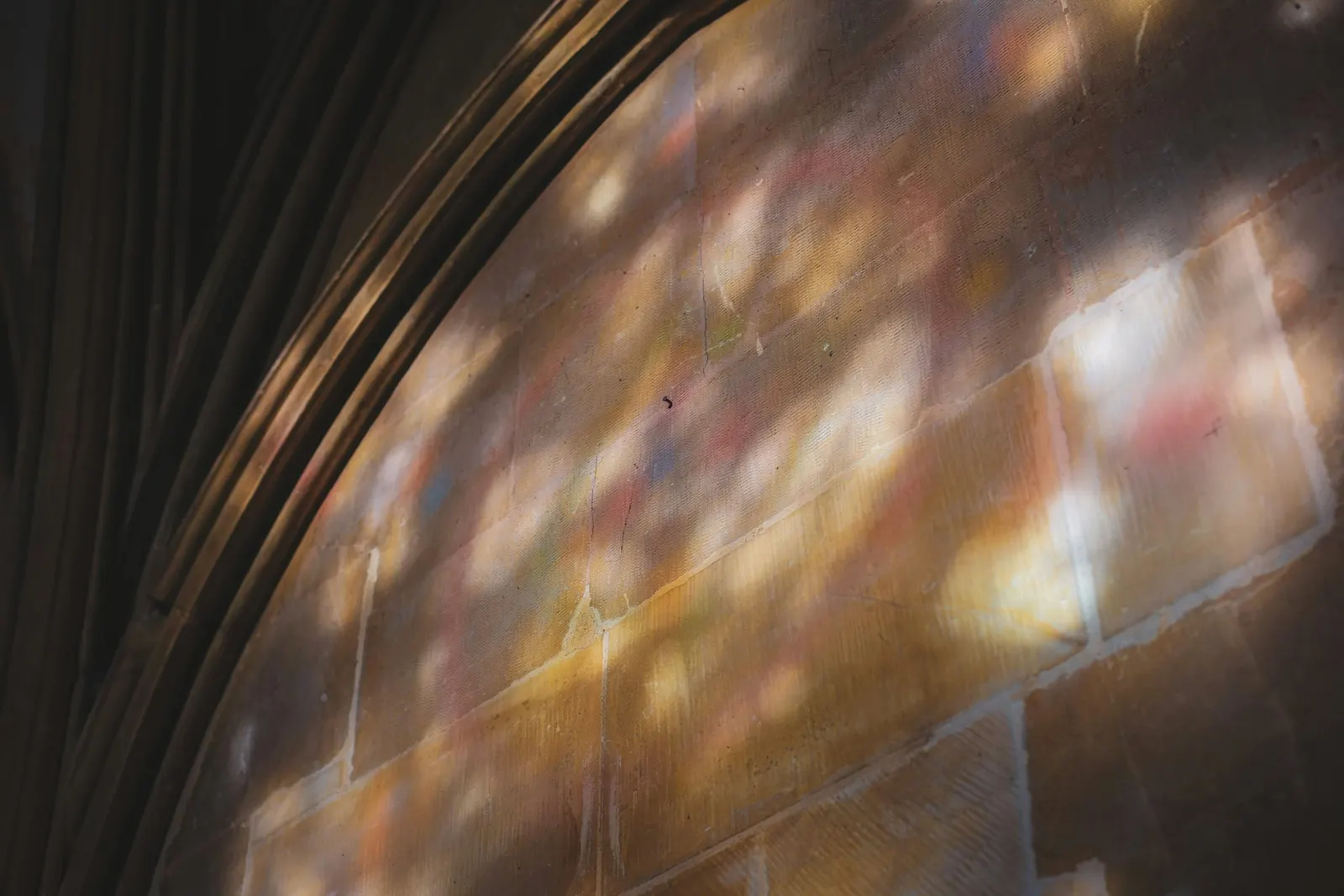 Soft colored light from stained glass falling across a stone arch