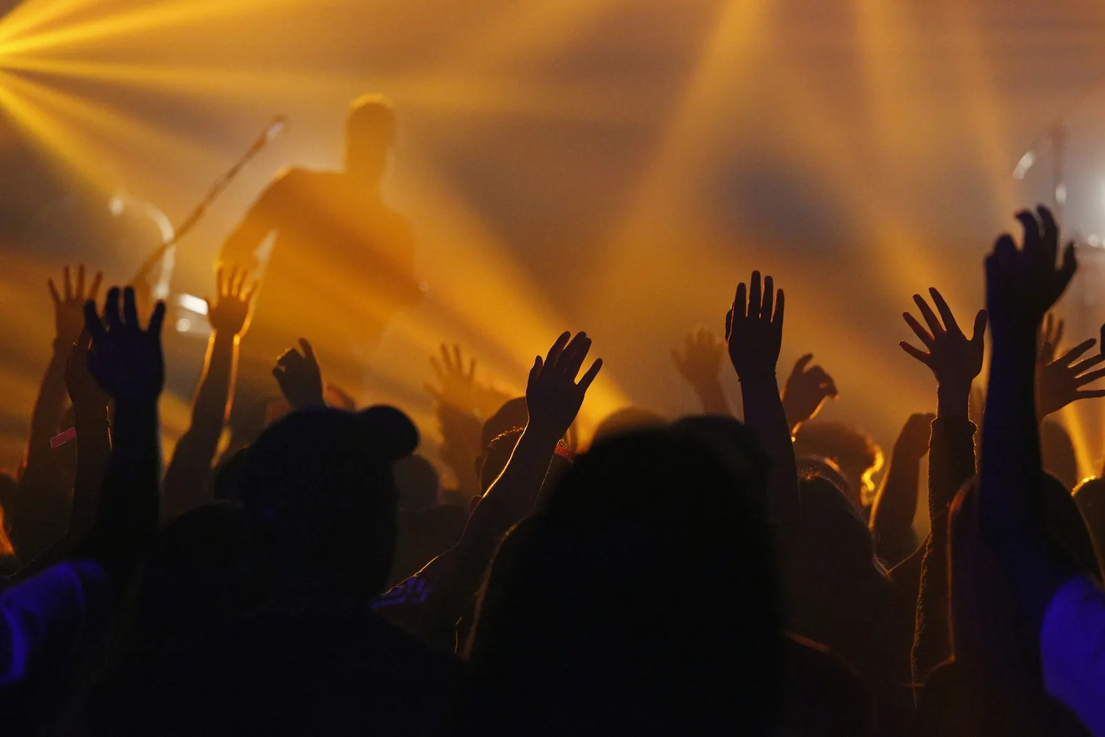 a crowd raising hands in silhouette as golden stage light streams over a performer
